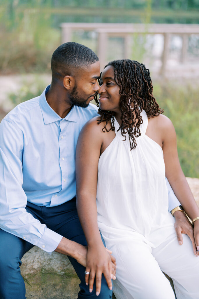 gnes and Uzo sit close together on a large boulder by the water, snuggled up next to each other during their engagement session at Union Grove Barn in Chapel Hill, North Carolina, captured by North Carolina wedding photographer Jessica Leigh Mason.