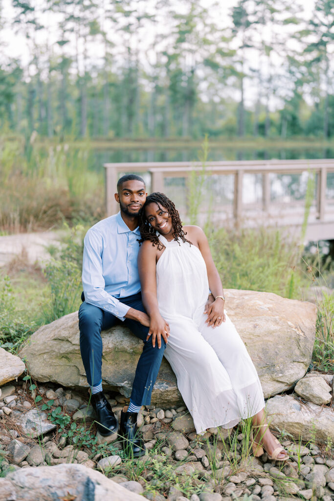 Agnes and Uzo sit closely together on a boulder beside the water at Union Grove Barn in Chapel Hill, North Carolina, enjoying a quiet, intimate moment captured by Durham wedding photographer Jessica Leigh Mason.