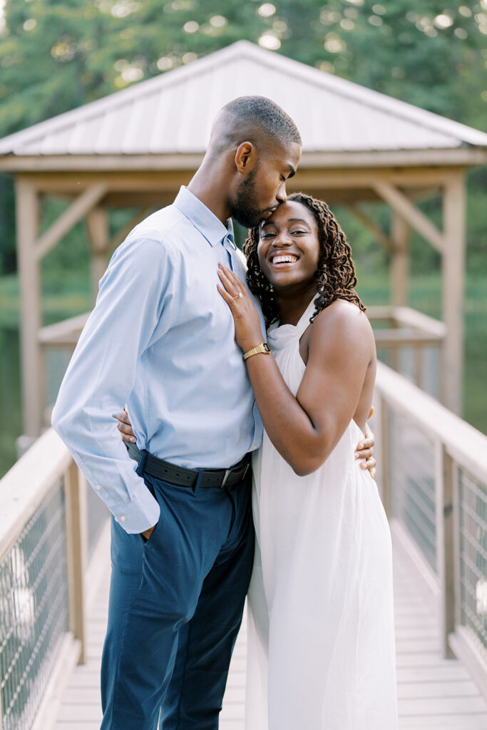 Uzo kisses Agnes’s forehead while she smiles happily at the camera during their engagement session at Union Grove Barn in Chapel Hill, North Carolina, captured by North Carolina wedding photographer Jessica Leigh Mason.