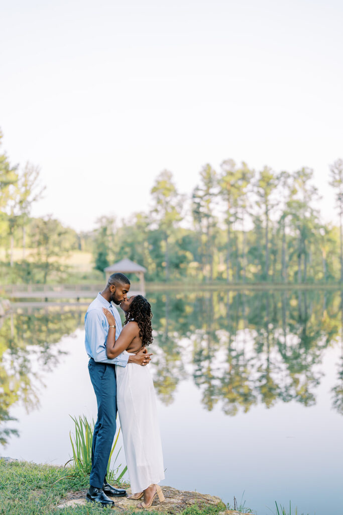 Agnes and Uzo share a romantic kiss beside the still, mirror-like lake at Union Grove Barn in Chapel Hill, North Carolina, beautifully captured by Durham wedding photographer  Jessica Leigh Mason.