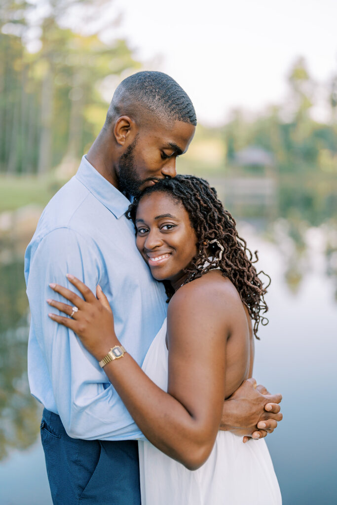 Agnes and Uzo share a sweet embrace with the peaceful lake and white gazebo in the background at Union Grove Barn in Chapel Hill, North Carolina, captured by Durham wedding photographer Jessica Leigh Mason.