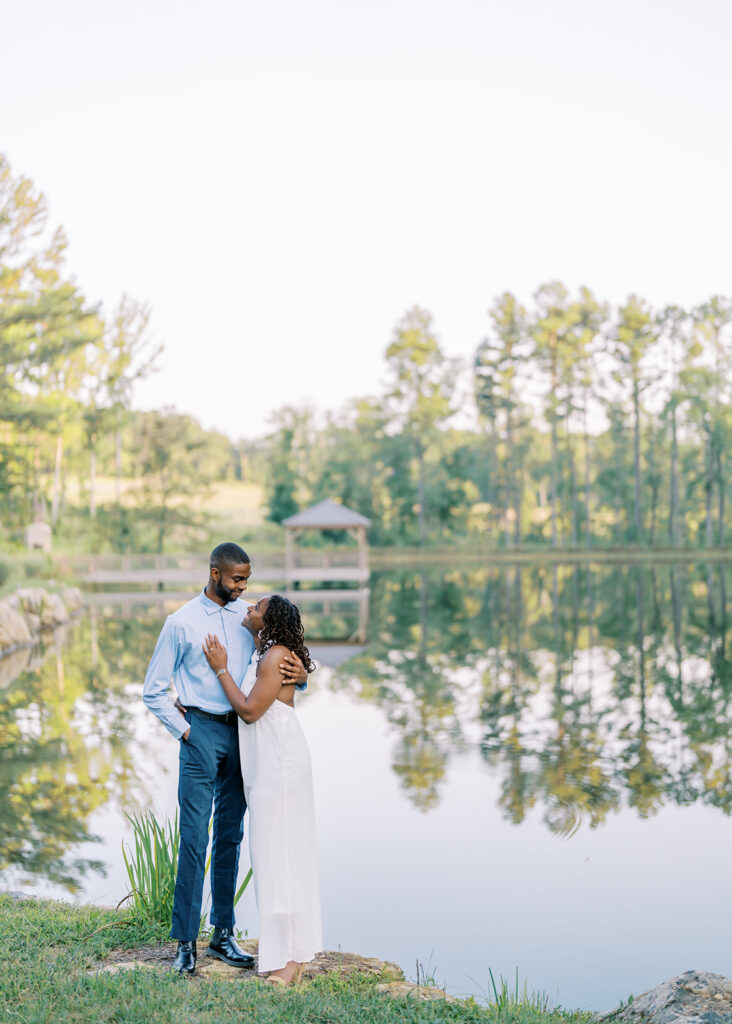 Agnes and Uzo stand together by the beautifully reflective lake at Union Grove Barn in Chapel Hill, North Carolina, with soft scenery mirrored on the water, captured by North Carolina wedding photographer Jessica Leigh Mason.

