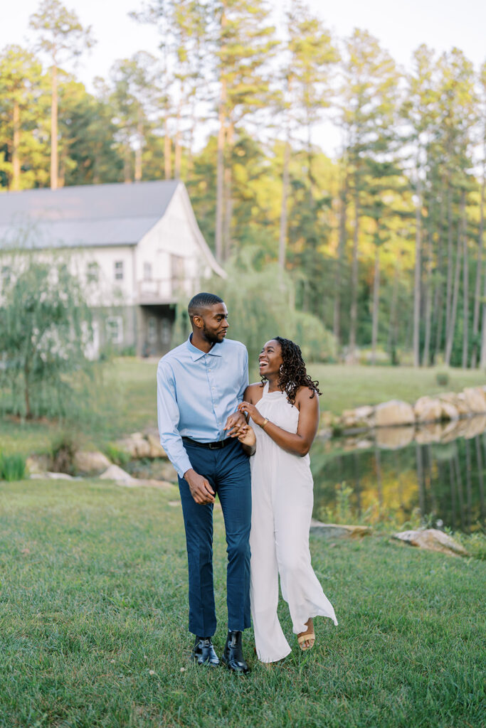 A candid moment as Agnes and Uzo laugh together with the serene lake and charming wedding barn at Union Grove Barn in Chapel Hill, North Carolina in the backdrop, captured by North Carolina wedding photographer Jessica Leigh Mason.