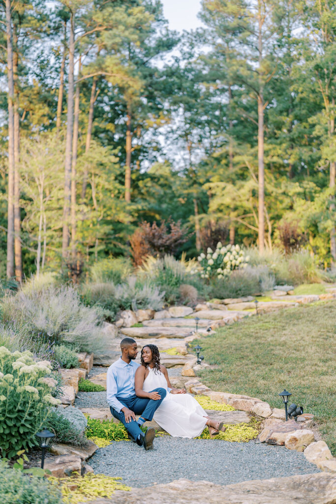 Agnes and Uzo sit together on the stairs beside a lush, green garden at Union Grove Barn in Chapel Hill, North Carolina, captured by North Carolina wedding photographer Jessica Leigh Mason.