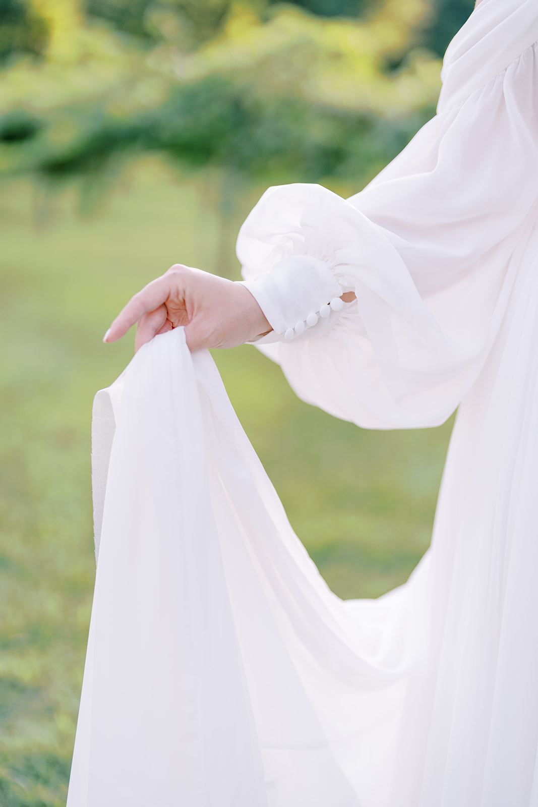 The bride holds up her flowing gown, showcasing romantic billowing long sleeves during her bridal session at The Vines of Lexington in South Carolina, captured by North Carolina wedding photographer Jessica Leigh Mason.