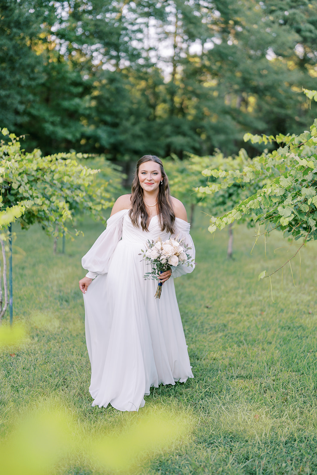 A joyful bride-to-be smiles in a romantic off-shoulder wedding dress during her bridal session at The Vines of Lexington in South Carolina, captured by North Carolina wedding photographer Jessica Leigh Mason.