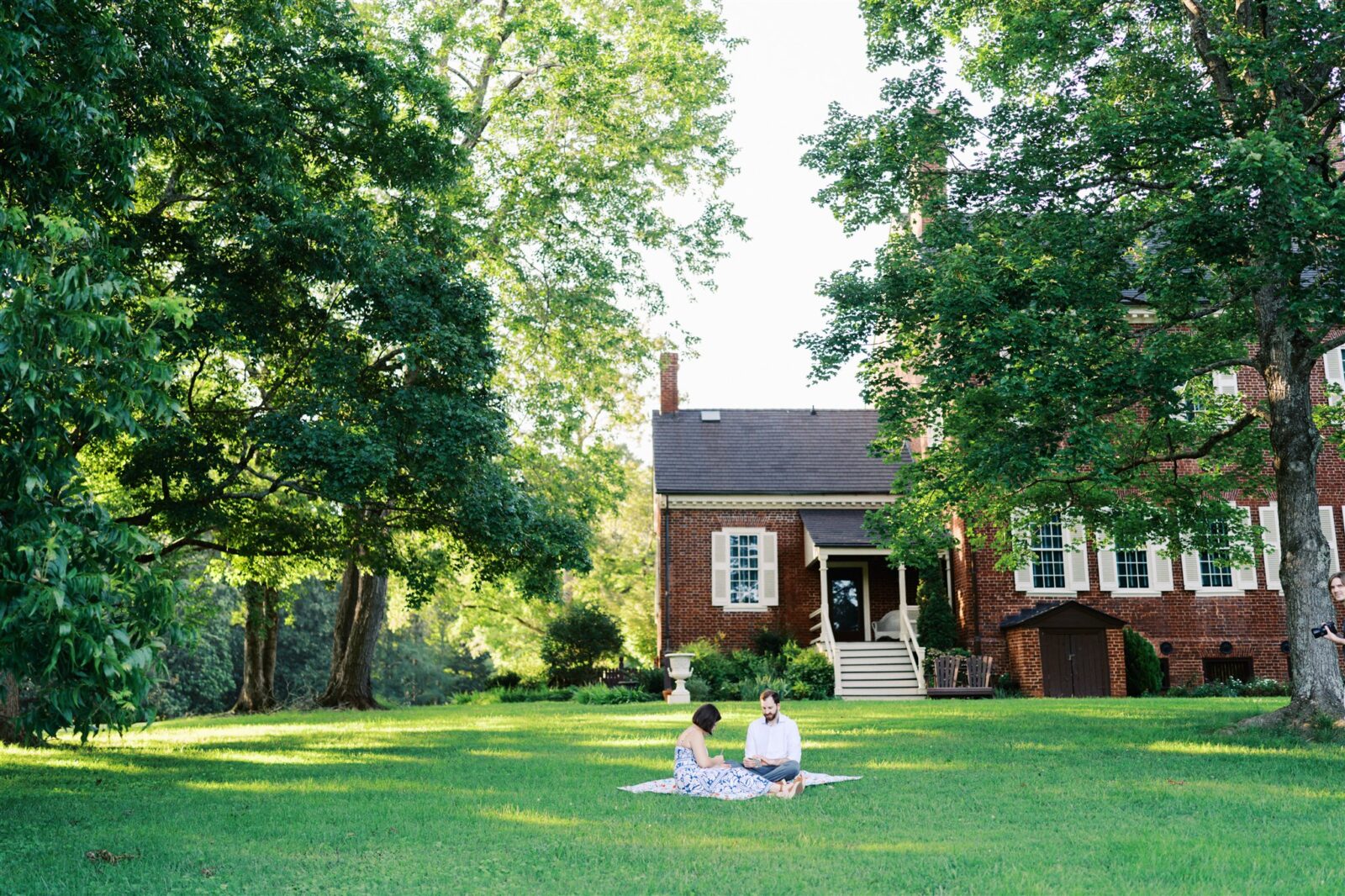 Katie and Sam enjoying a picnic together at Ayr Mount in Hillsborough NC during their anniversary photo session, capturing a relaxed and joyful moment.