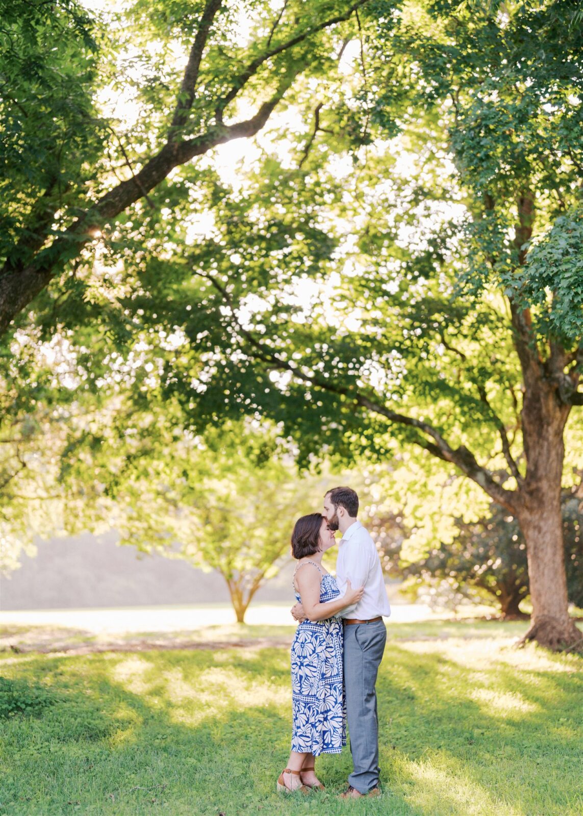 Katie and Sam sharing a gentle forehead kiss under a tree canopy at Ayr Mount in Hillsborough NC during their anniversary photo session.