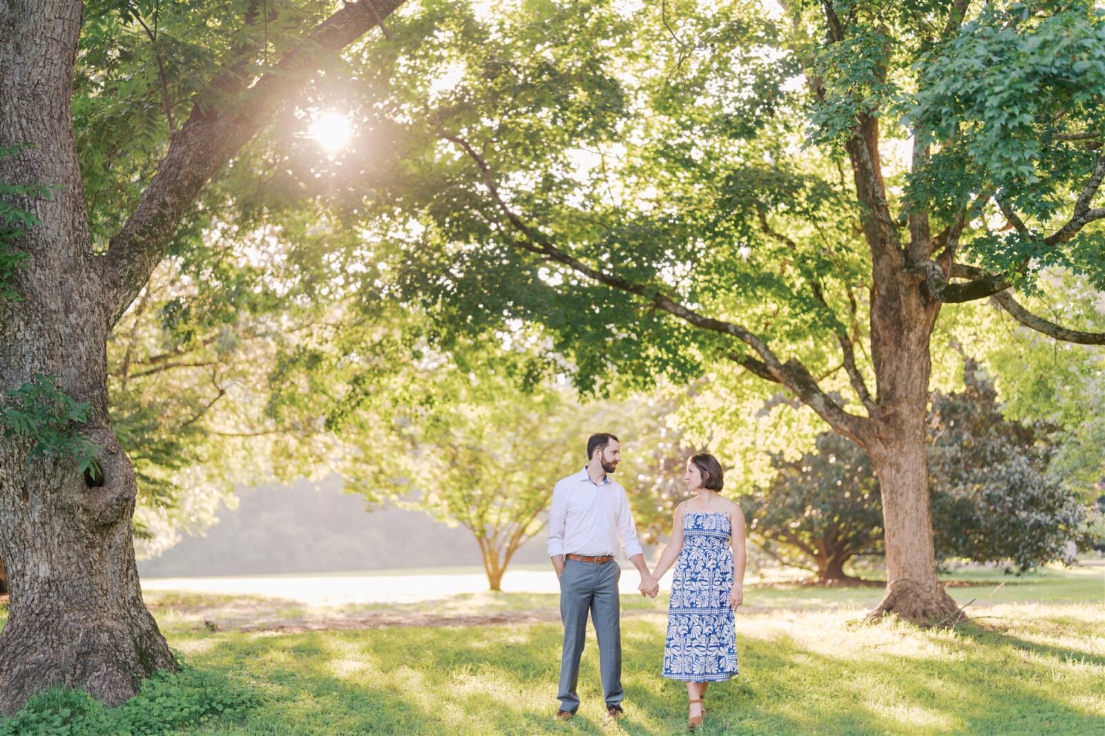 Katie and Sam holding hands while walking through the trees at Ayr Mount in Hillsborough NC, surrounded by golden hour light during their anniversary photo session.