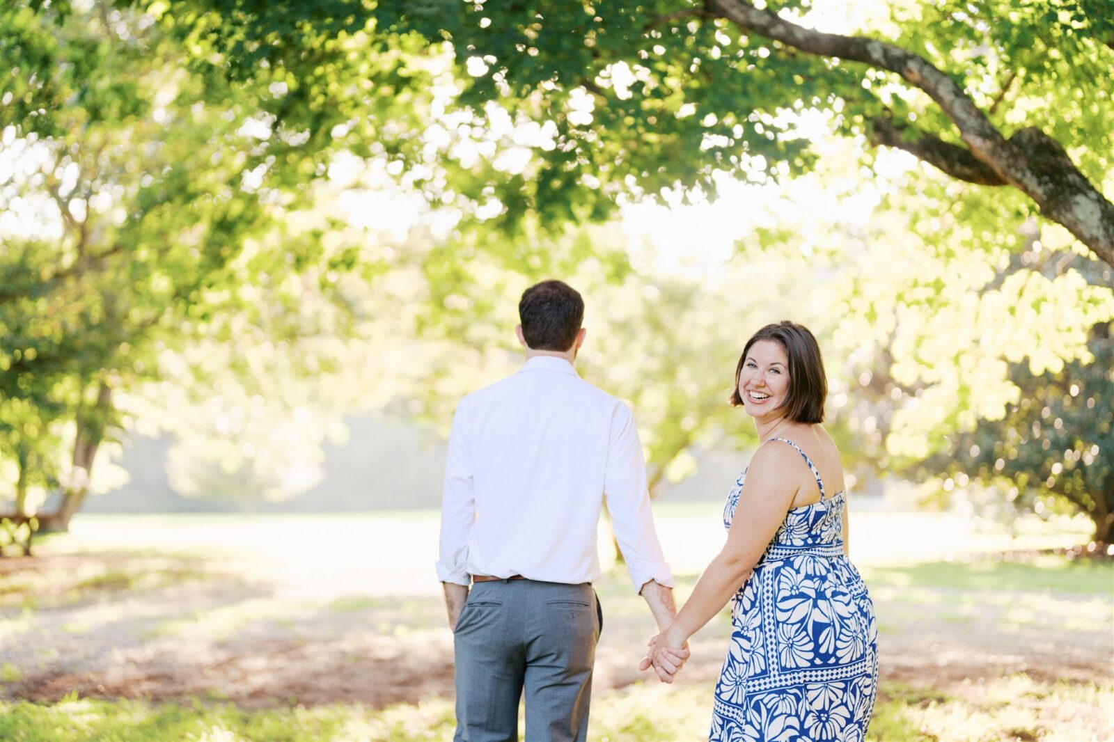 Katie turns to look at the camera while walking hand in hand with Sam at Ayr Mount in Hillsborough NC during their anniversary photo session.