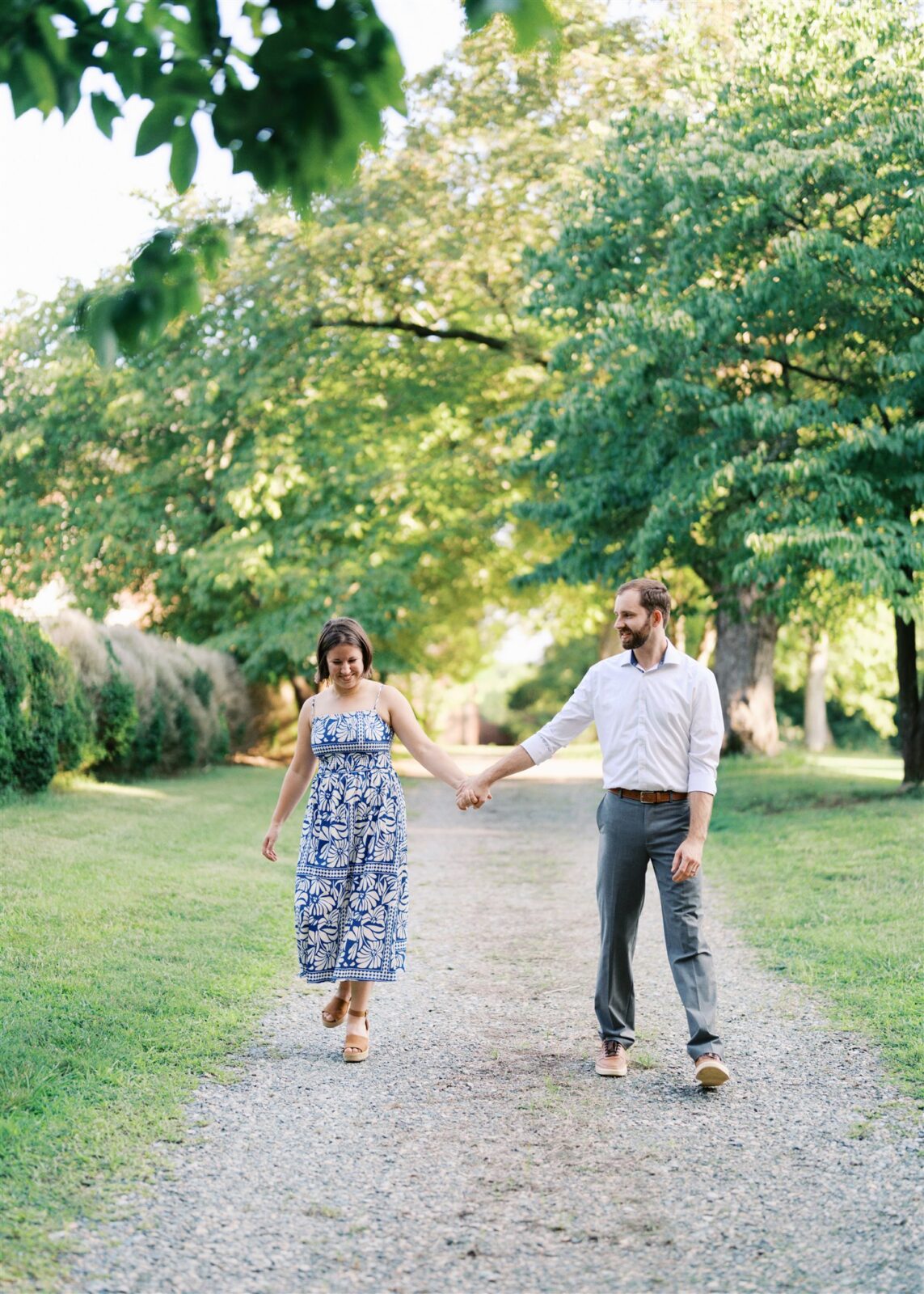 Katie and Sam walking down a covered, tree-lined path at Ayr Mount in Hillsborough NC during their anniversary photo session, surrounded by lush greenery.