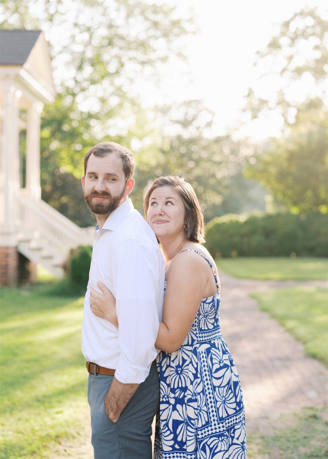 Katie and Sam posing playfully with a backpack during their anniversary photo session at Ayr Mount in Hillsborough NC, capturing their joyful personalities.