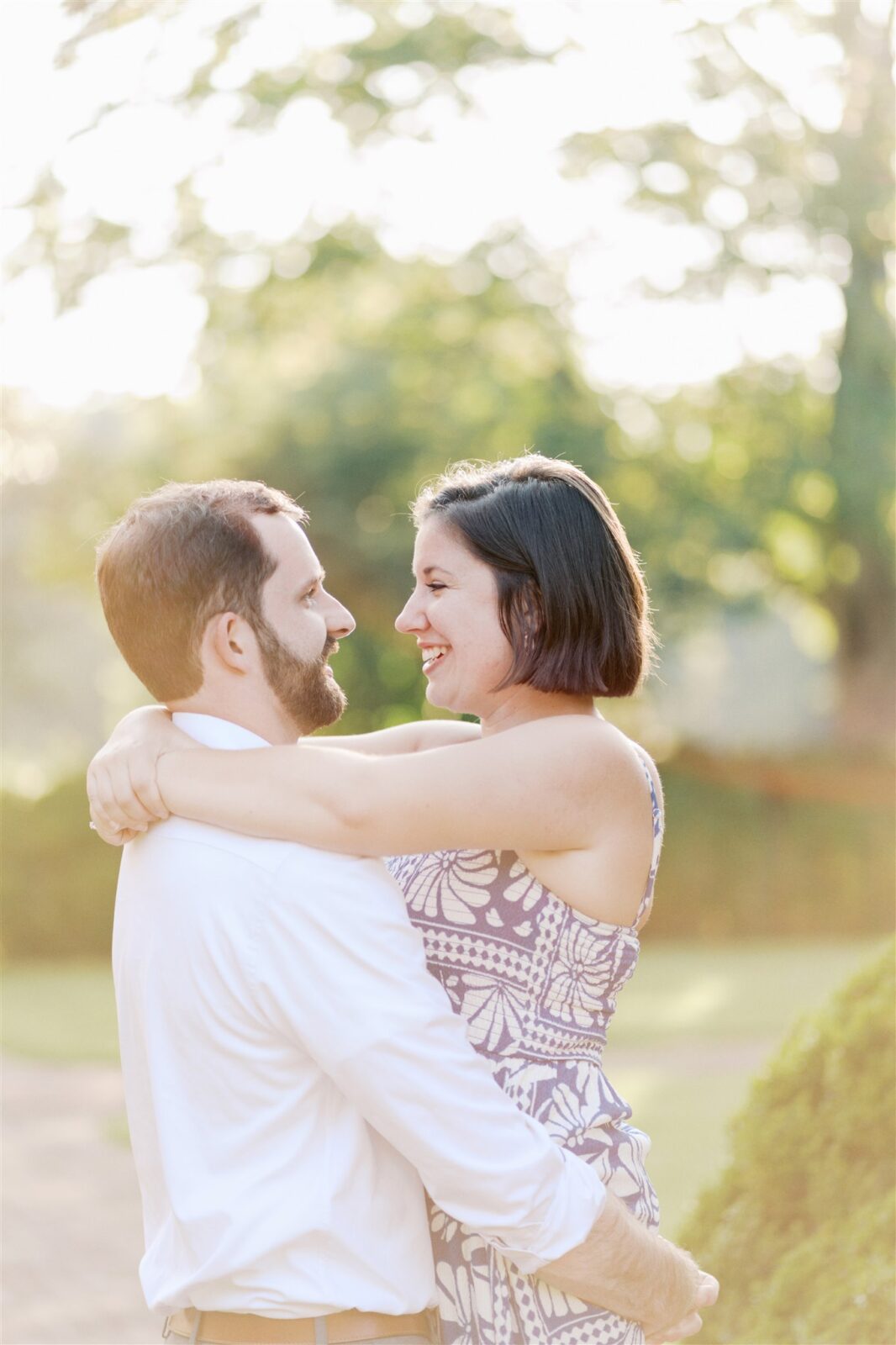 Sam carrying Katie in golden hour light during their fine-art anniversary photo session at Ayr Mount in Hillsborough NC, capturing a joyful and romantic moment.