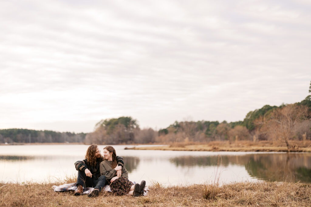 Winter Engagement Session at Lake Crabtree | Raleigh NC A couple sits together near the water at Lake Crabtree in Raleigh, North Carolina during a winter engagement session with soft, moody light, captured by North Carolina wedding photographer Jessica Leigh Mason.