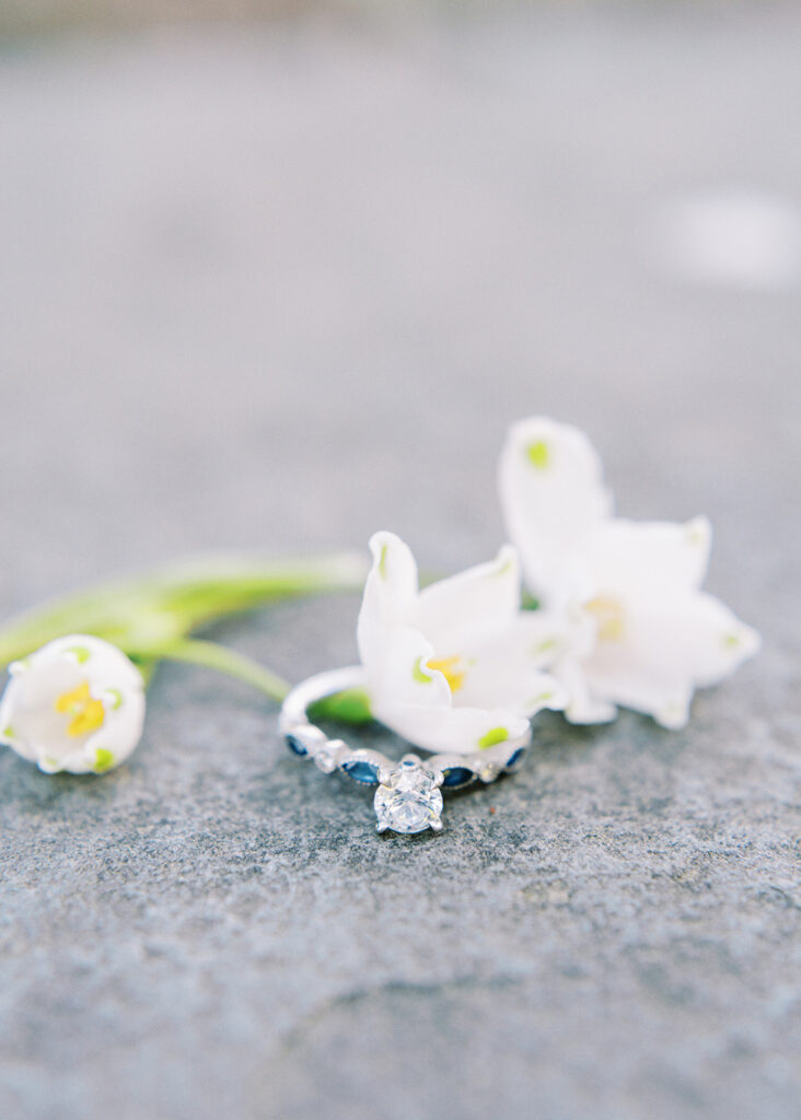 Engagement ring with sapphire details surrounded by spring flowers during a Charlotte, North Carolina engagement session at Romare Bearden Park