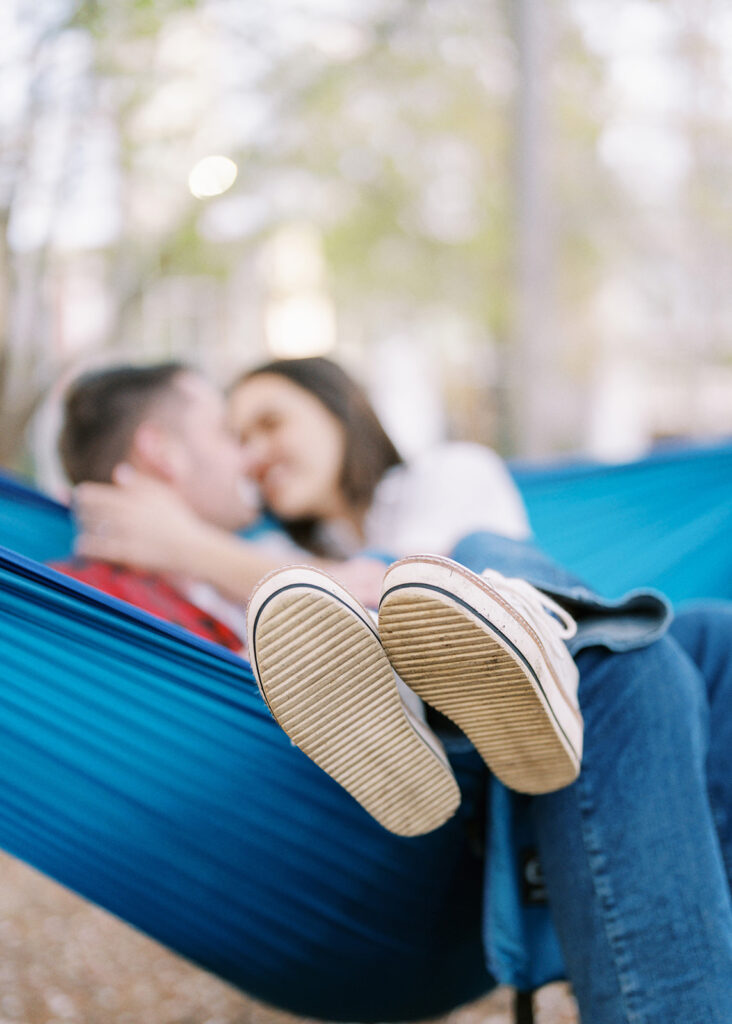 Close-up of a couple snuggled together in a hammock, showing their Converse shoes during an engagement session at Romare Bearden Park in Charlotte, North Carolina