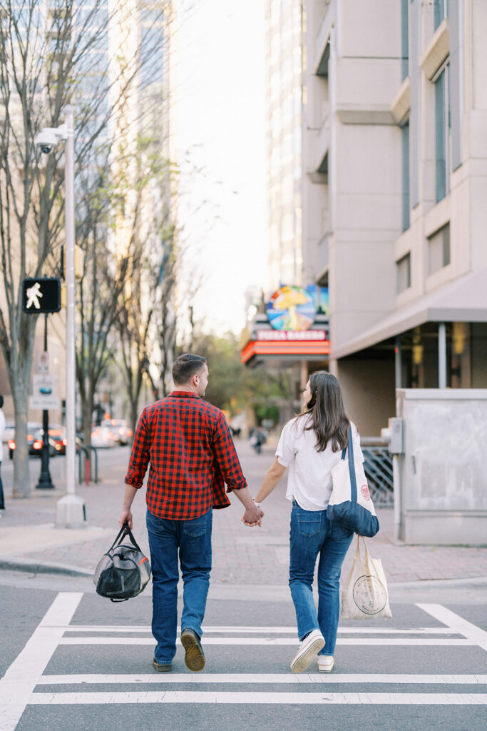 Engaged couple walking across the street hand in hand in uptown Charlotte
