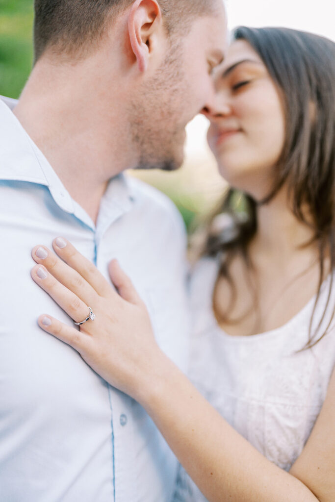 Couple almost kissing with her hand resting on his chest, featuring her sapphire engagement ring, captured at Romare Bearden Park in Charlotte, North Carolina