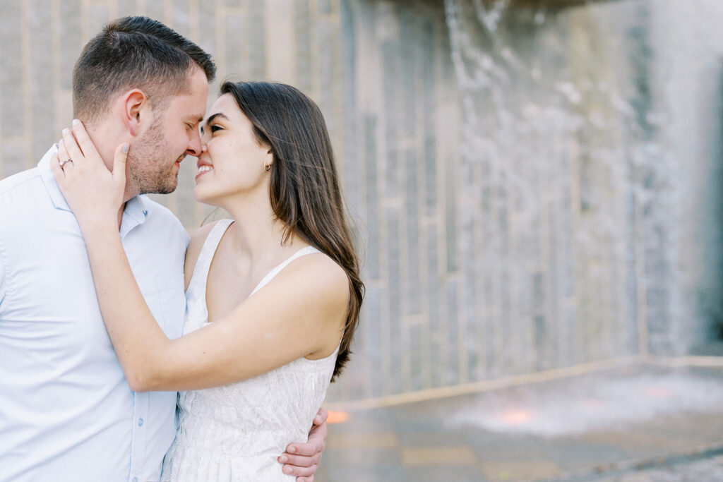 Couple embracing in front of a waterfall at Romare Bearden Park in Charlotte, North Carolina during their engagement session