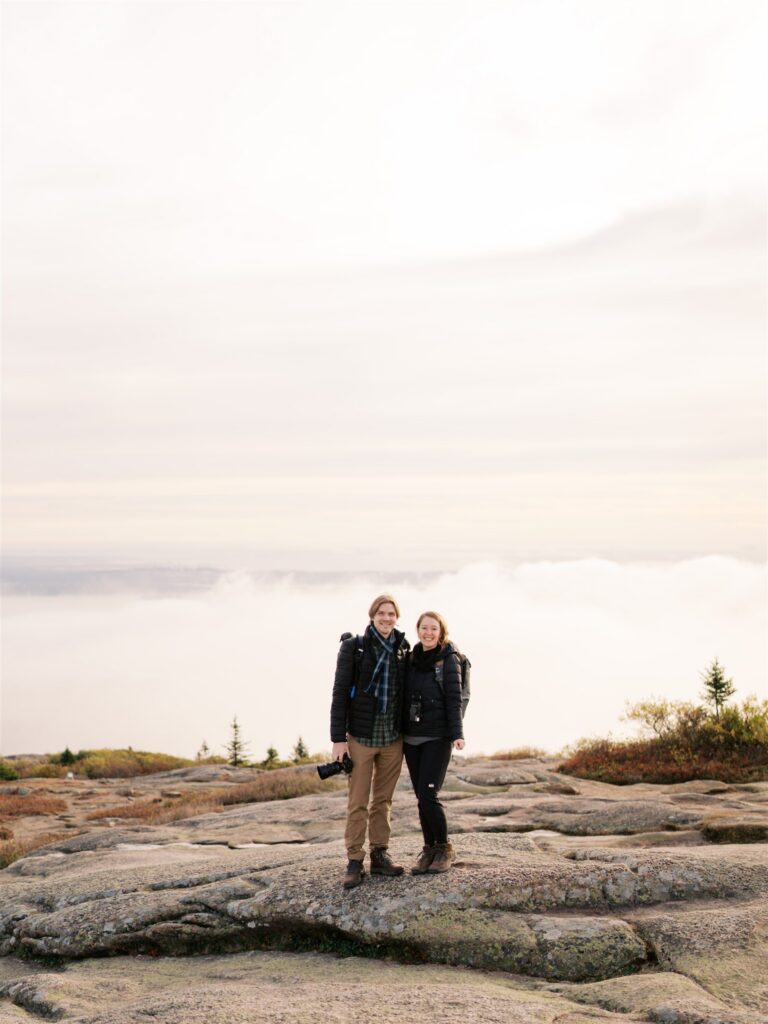 Couple smiling together in the moody fog on Cadillac Mountain in Acadia Maine — a dreamy engagement session location

