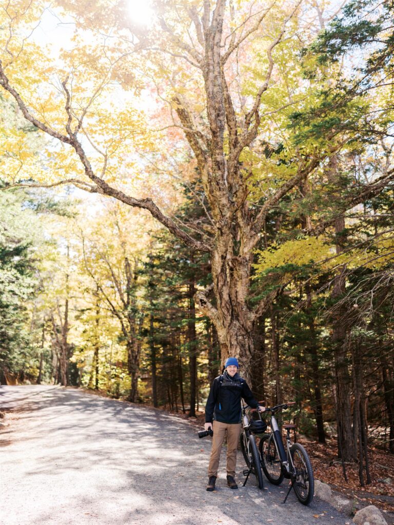 Cyclist pausing on the carriage roads in Acadia with a raven perched nearby
