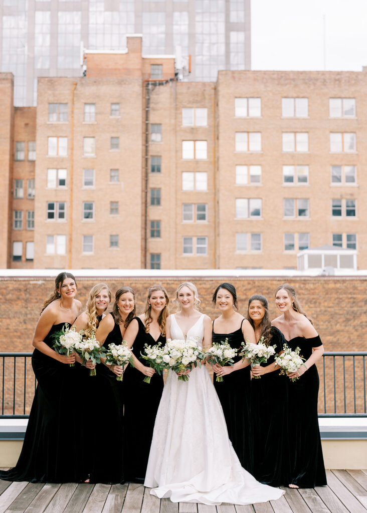 Bridal party laughing and celebrating on a rooftop with downtown Raleigh skyline behind them