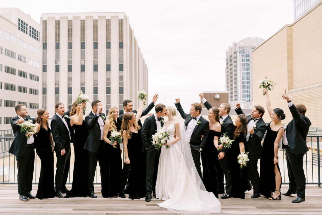 Bridal party cheering as the couple shares a kiss with downtown Raleigh behind them