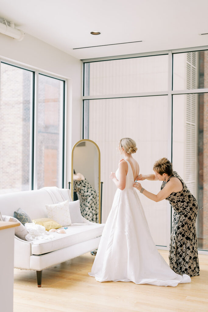 Candid moment of a bride being dressed by her mother in a bridal suite