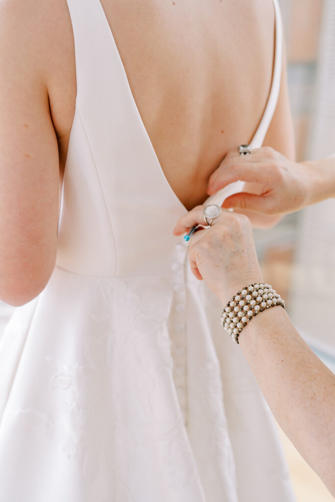 Close-up of wedding dress being fastened with buttons on the back