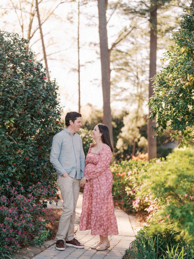 Expecting mom and dad holding hands together along the path at WRAL Azalea Gardens Raleigh NC