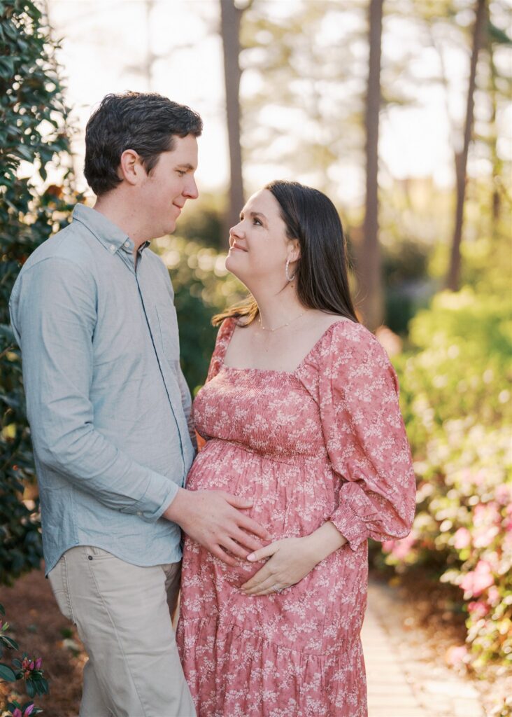 Expecting couple embracing with hands on baby bump at WRAL Azalea Gardens Raleigh NC during spring maternity session