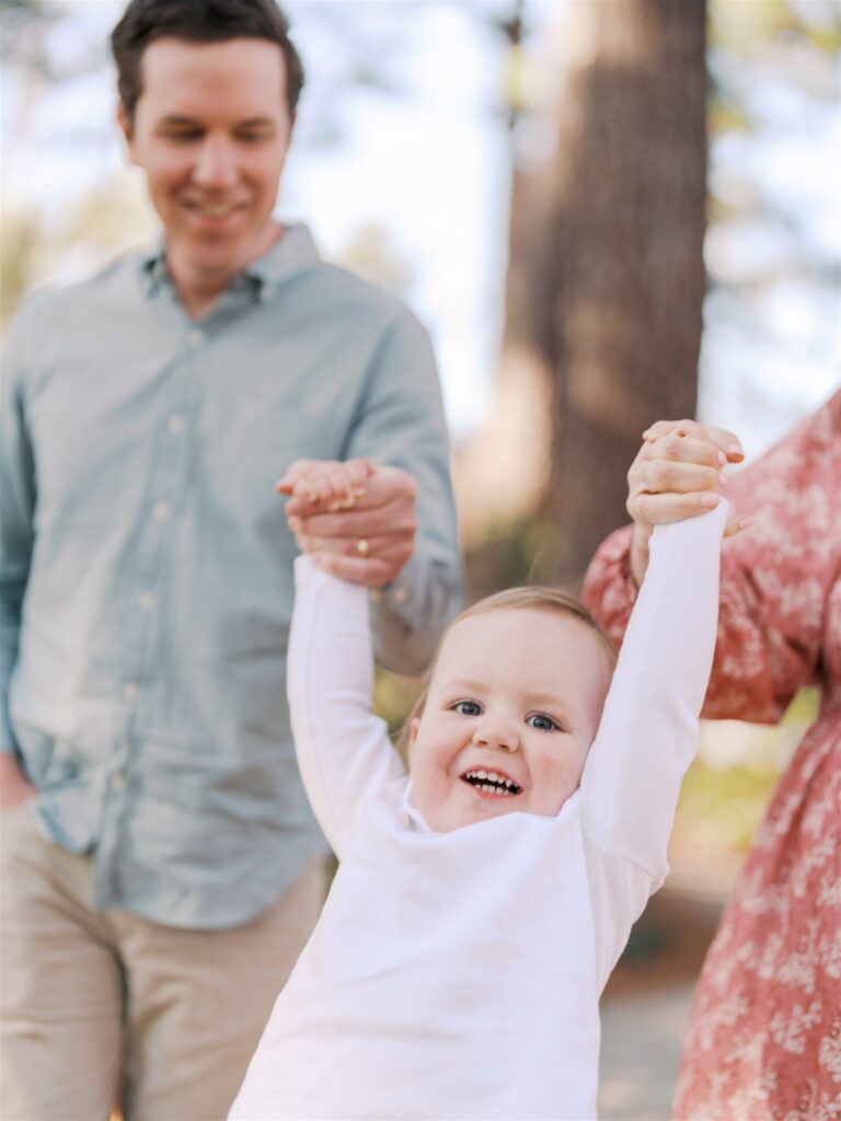 Parents swinging toddler by the hands while walking at WRAL Azalea Gardens Raleigh NC