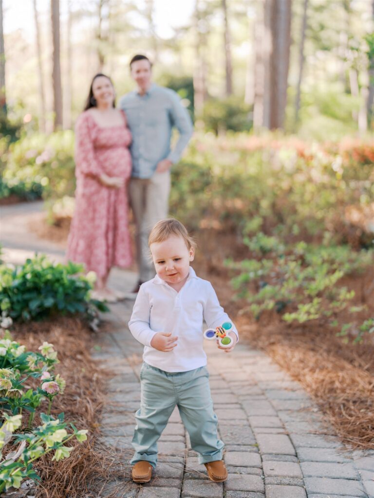 oddler walking away as a distraction during family maternity photos at WRAL Azalea Gardens Raleigh NC