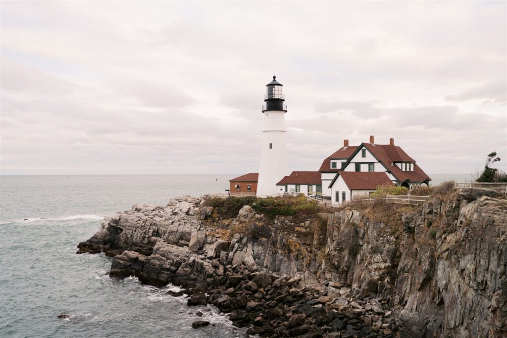 Wide angle view of Portland Head Light from the western shore with dramatic rocky coastline and open Atlantic sky in Cape Elizabeth Maine