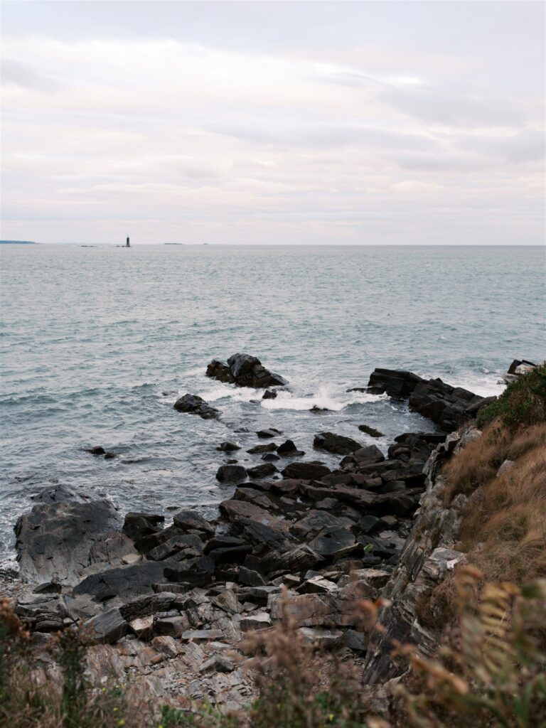 Vivid blue Atlantic water meeting the rugged rock formations along the coastal shoreline at Portland Head Light Maine