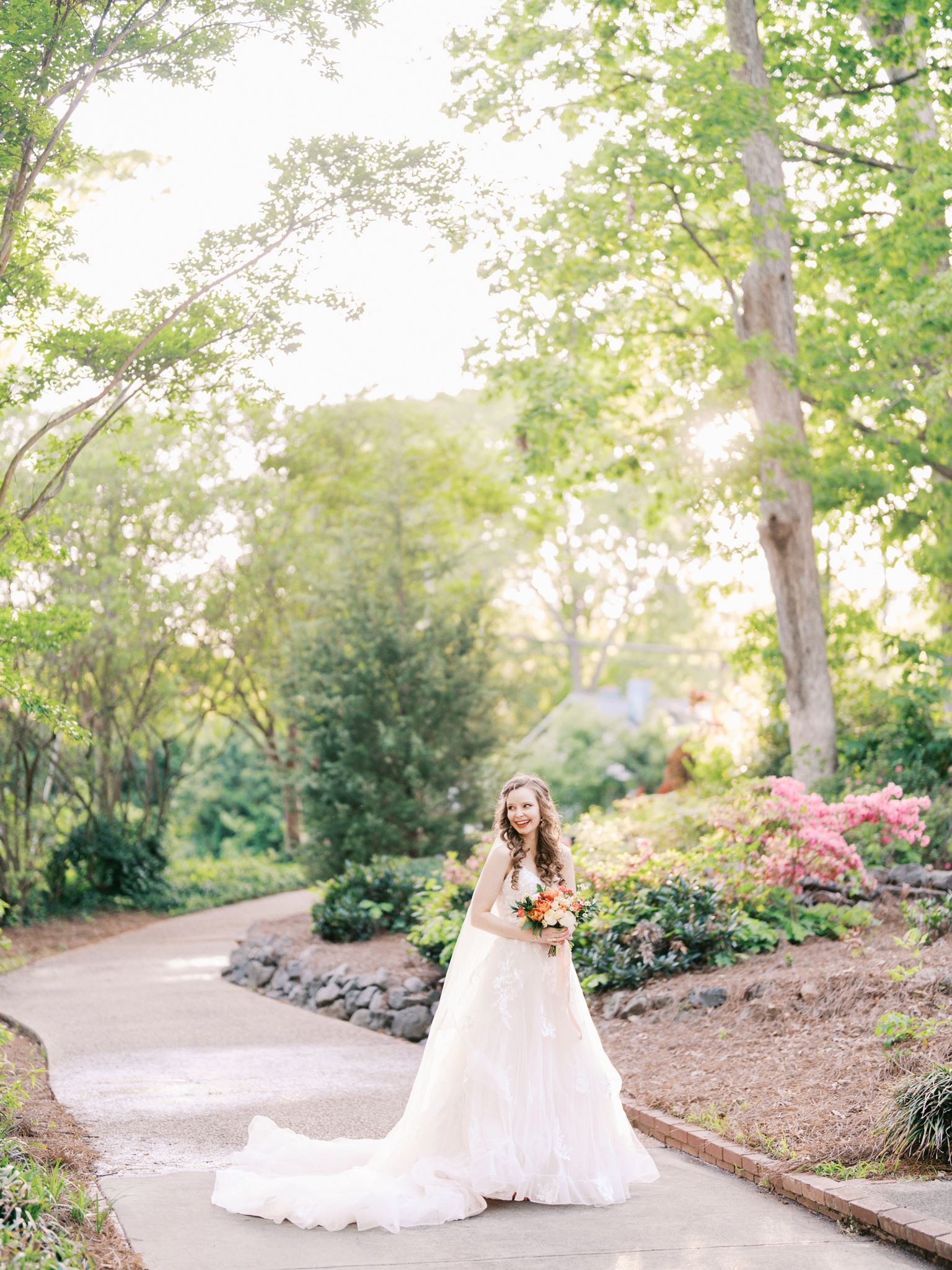 Bride standing on a flower-lined path with bright spring light during a Glencairn Garden bridal portrait session