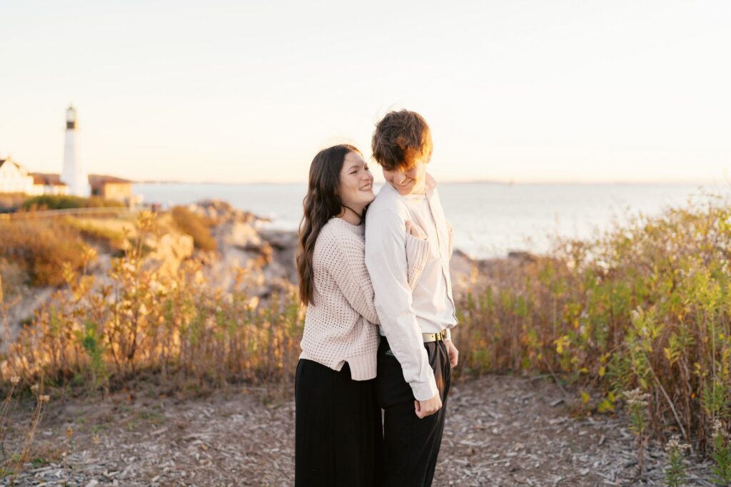 Engaged couple laughing during a playful piggyback ride at sunrise in Cape Elizabeth, Maine