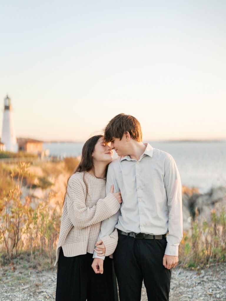 Engaged couple sharing a quiet moment with the iconic Maine lighthouse behind them in Cape Elizabeth
