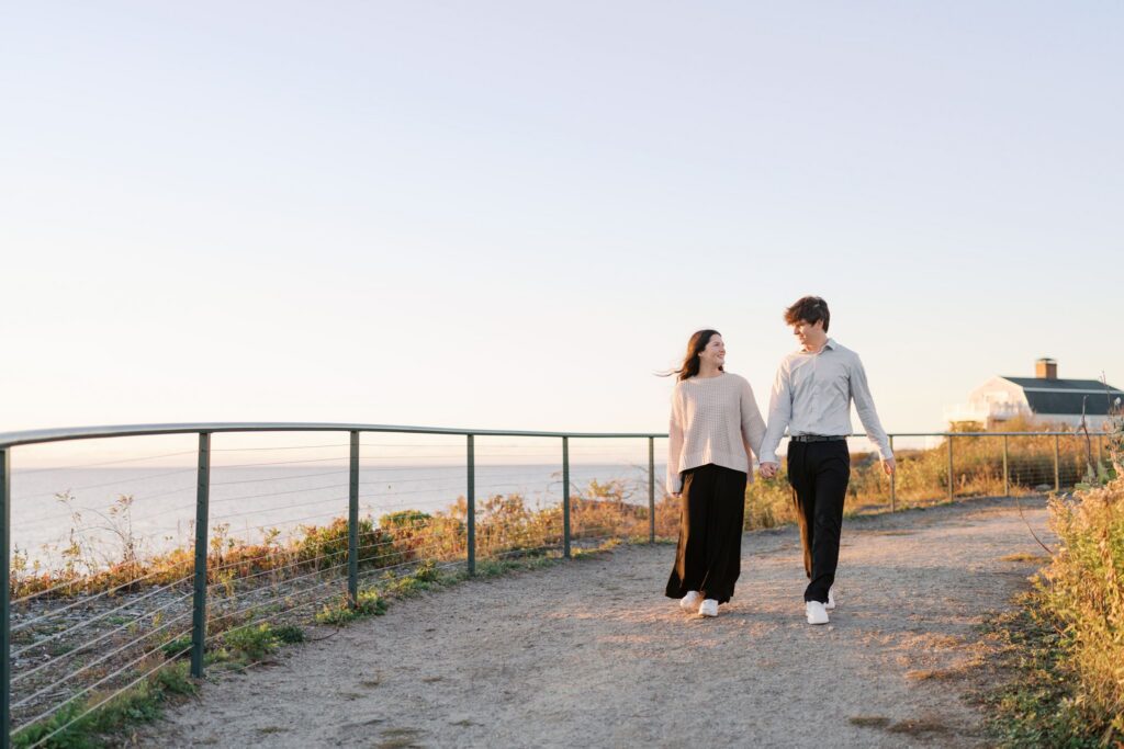 Engaged couple strolling together at sunrise near Portland Head Light in Cape Elizabeth, Maine