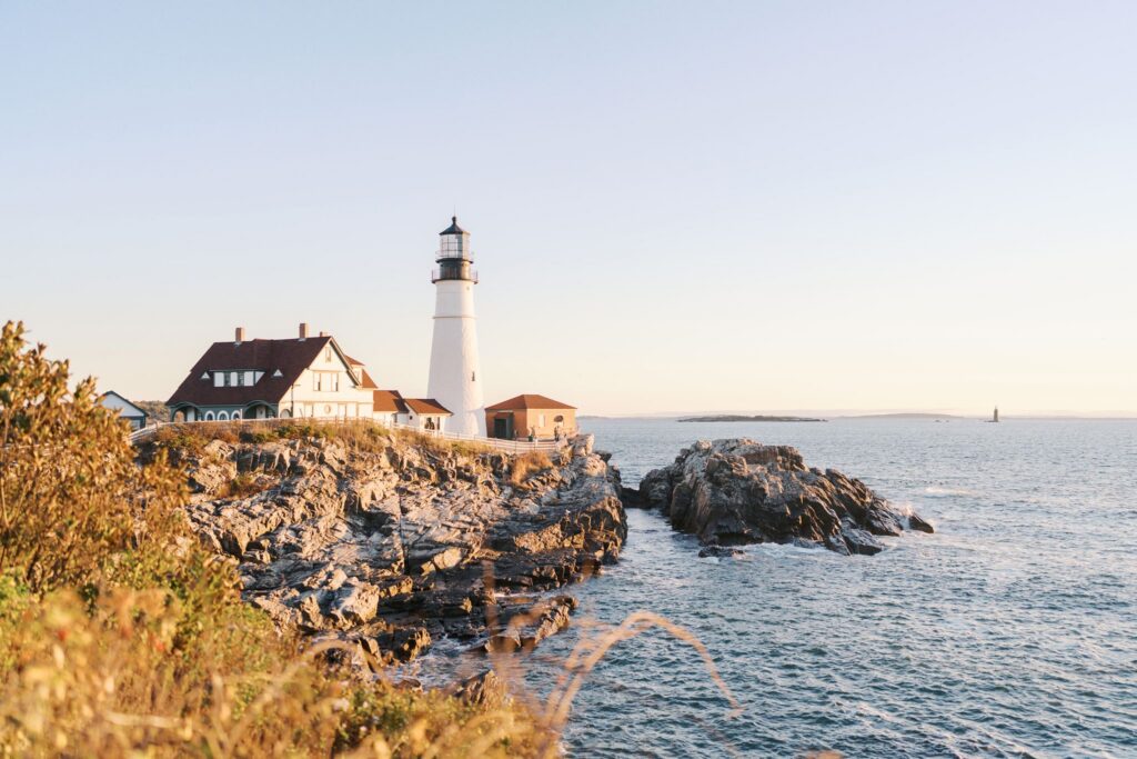 Portland Head Light lighthouse glowing at sunrise along the rocky Maine coastline in Cape Elizabeth
