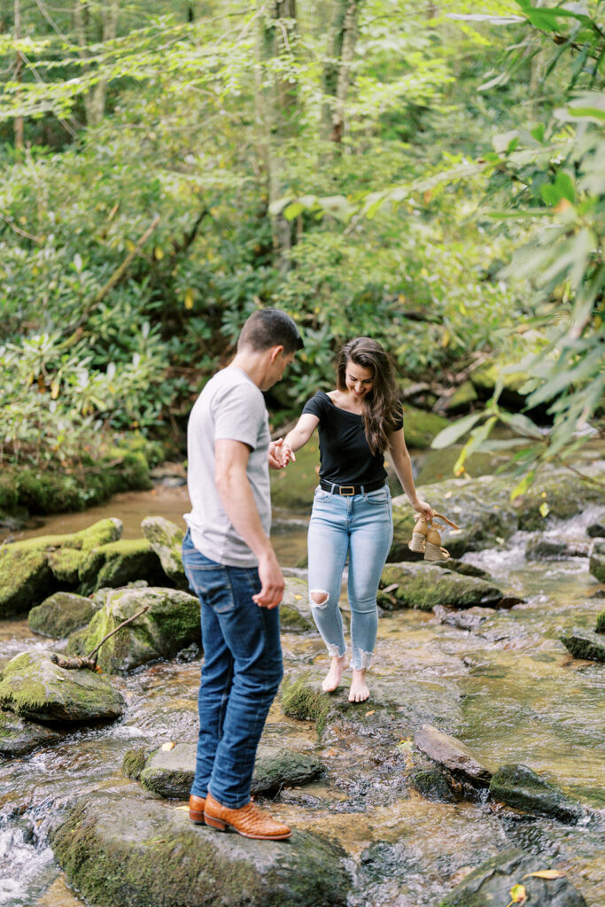 Man helping his fiancée cross the creek at their Blue Ridge Parkway engagement session near Boone, NC