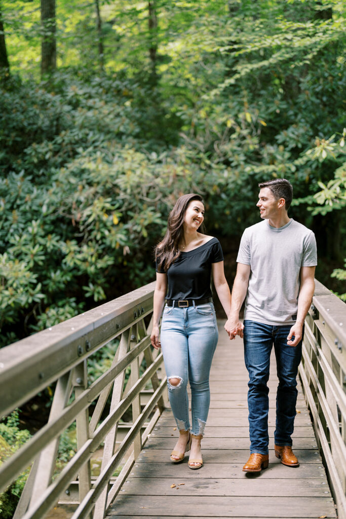 Engaged couple strolling across a bridge by the creek at their Blue Ridge Parkway engagement session near Boone, NC