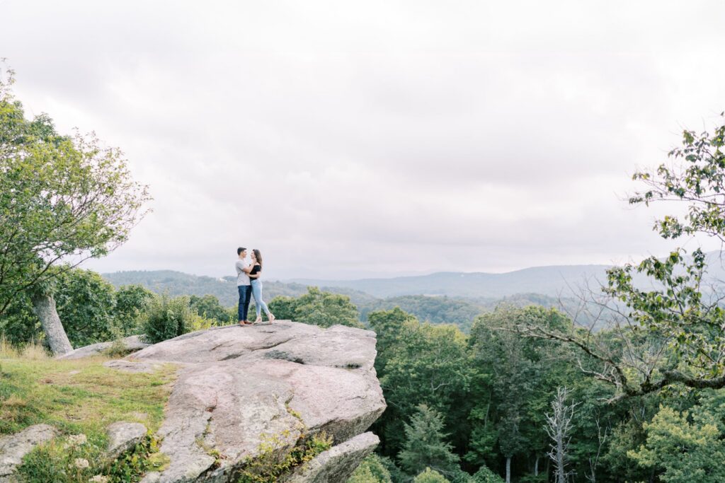 Engaged couple embracing, small against the sweeping landscape at Raven Rocks on the Blue Ridge Parkway near Boone, NC